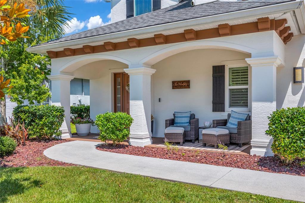 A covered front porch features white columns, wicker chairs with ottomans, and a wooden sign — 6835 STONEHEATH LANE, PORT ORANGE, FL