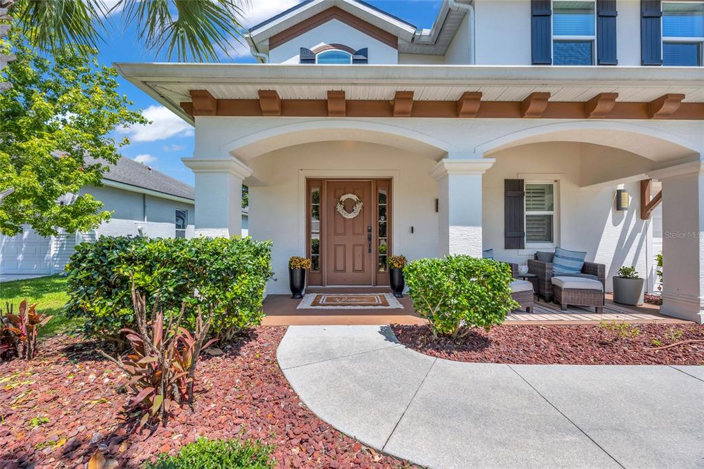 A covered front porch with a brown door, landscaping, and outdoor seating area — 6835 STONEHEATH LANE, PORT ORANGE, FL