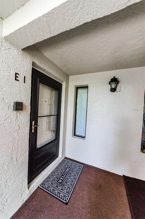 A front entryway features a dark door labeled E1, a welcome mat, and a wall lamp — 2575 PINE RIDGE WAY S UNIT E1, PALM HARBOR, FL