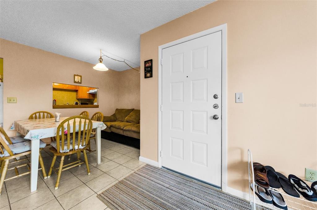 A dining area with tile flooring sits adjacent to an entryway with a white door — 2575 PINE RIDGE WAY S UNIT E1, PALM HARBOR, FL