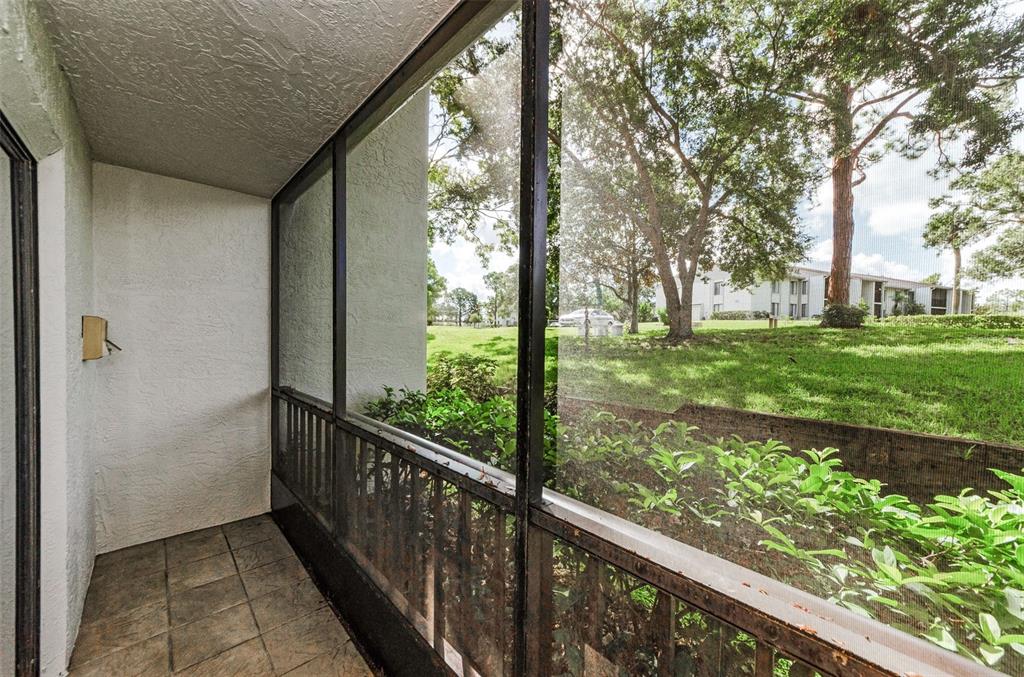 A screened-in patio with tiled flooring overlooks a grassy lawn and trees — 2575 PINE RIDGE WAY S UNIT E1, PALM HARBOR, FL