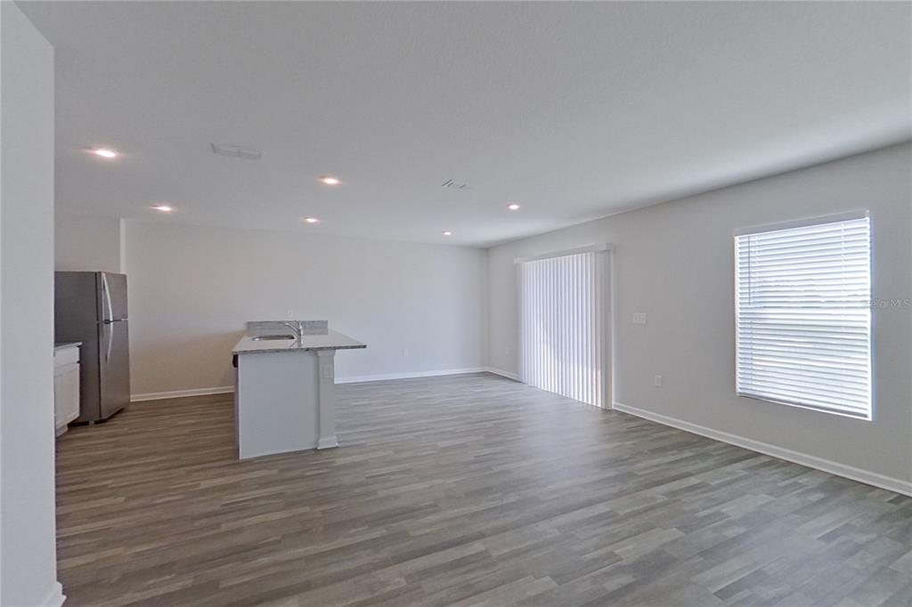 An open-concept kitchen and living area features light gray wood-look flooring and white walls — 1802 NEBRASKA LOOP, SUMTERVILLE, FL