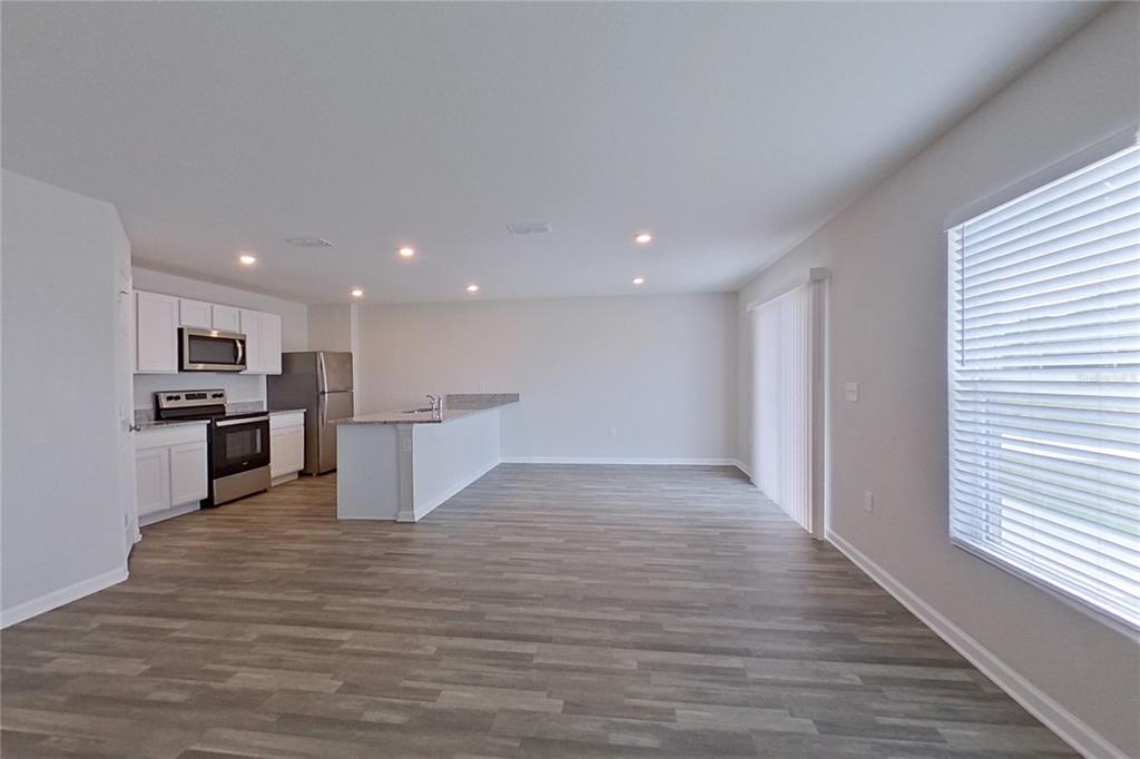 An open-concept kitchen and living area features white cabinets, stainless steel appliances, and wood-look flooring — 1802 NEBRASKA LOOP, SUMTERVILLE, FL