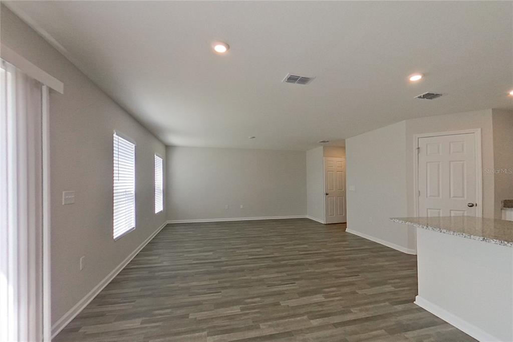 An empty living room features light gray walls, wood-look flooring, and a kitchen island — 1802 NEBRASKA LOOP, SUMTERVILLE, FL