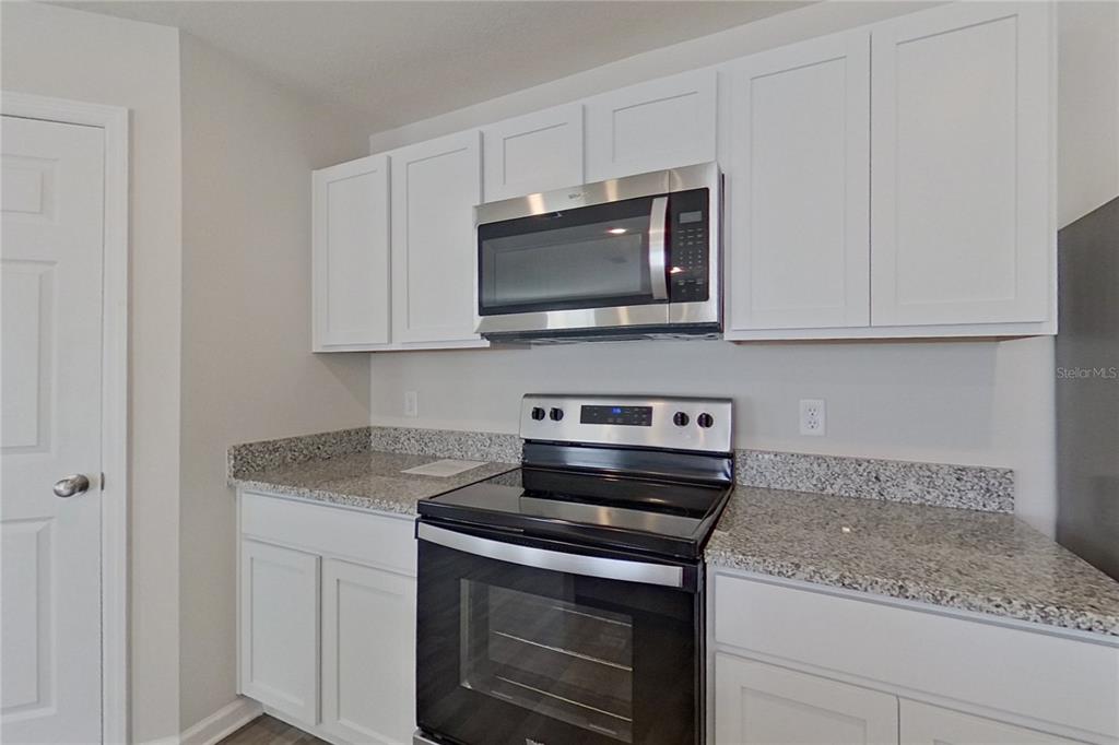 A kitchen features white cabinets, granite countertops, and stainless steel appliances — 1802 NEBRASKA LOOP, SUMTERVILLE, FL