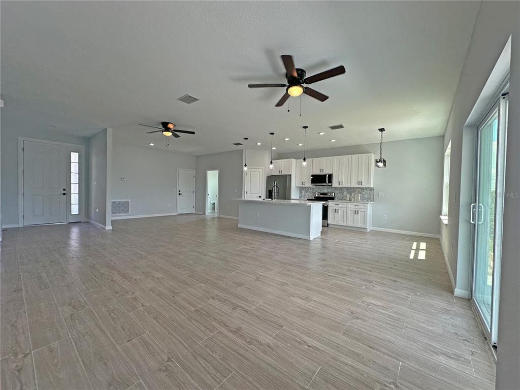 An open-concept kitchen and living area features light wood-look tile flooring and white cabinetry — 13558 JERONIMO LANE, PORT CHARLOTTE, FL