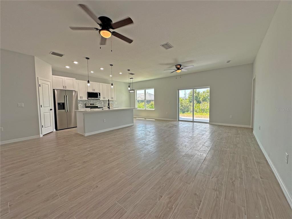 An open-concept kitchen and living area features light tile flooring, white cabinetry, and sliding doors — 13558 JERONIMO LANE, PORT CHARLOTTE, FL