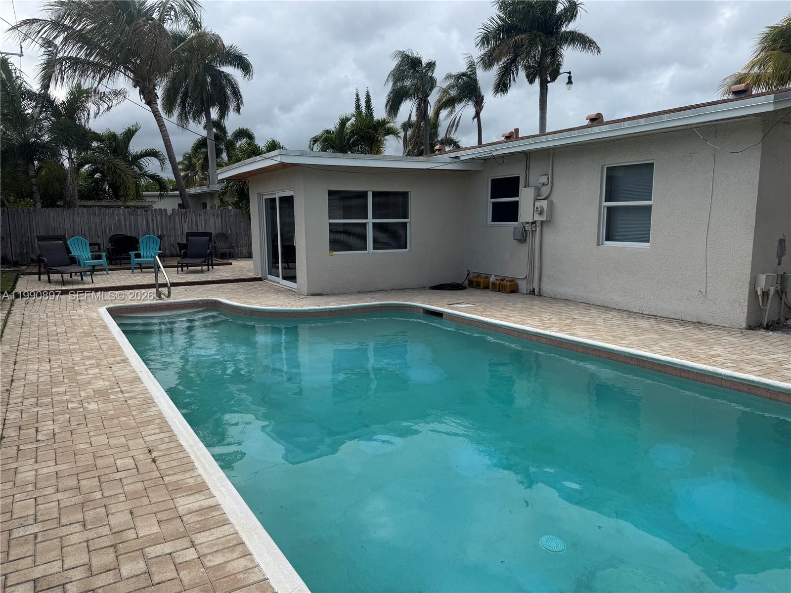 A backyard features a paved patio, a swimming pool, and outdoor furniture on a wooden deck — 1460 NE 30th Ct, Pompano Beach FL 33064, POMPANO BEACH, FL