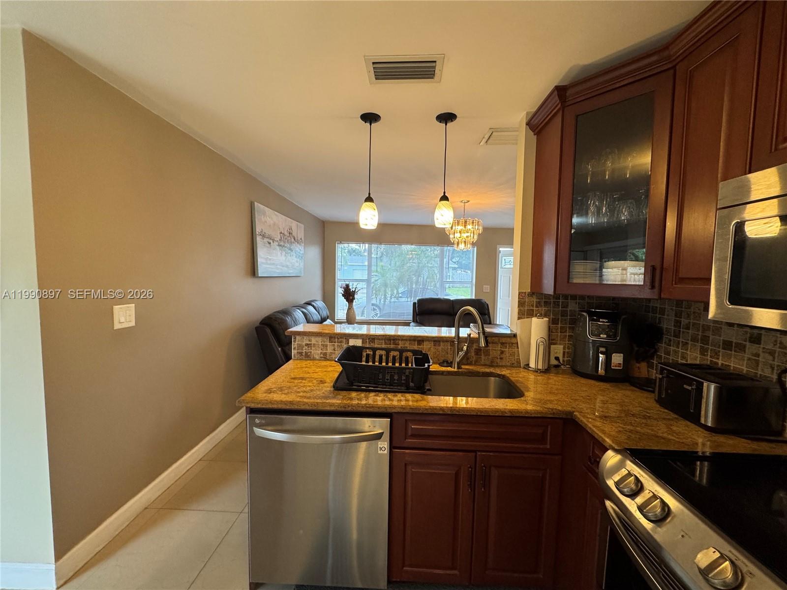 A kitchen with wood cabinets, stainless steel appliances, and granite countertops overlooks a living area — 1460 NE 30th Ct, Pompano Beach FL 33064, POMPANO BEACH, FL