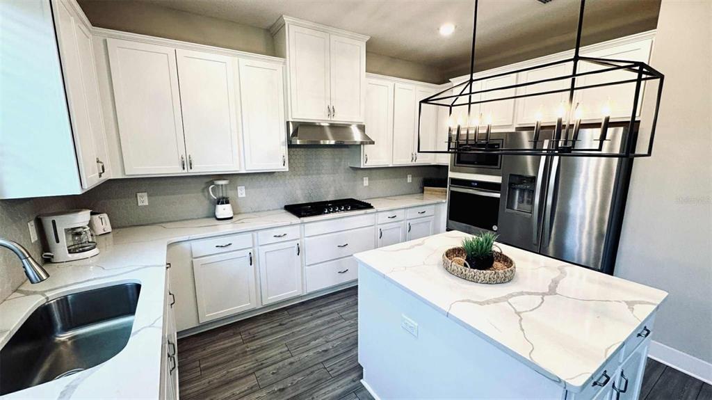 A modern kitchen features white cabinets, stainless steel appliances, and a quartz-topped center island — 7958 HAVERHILL WAY, KISSIMMEE, FL