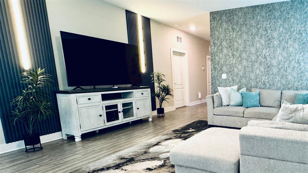 A living room features a large television on a white console, gray sofa, and accent wall — 7958 HAVERHILL WAY, KISSIMMEE, FL