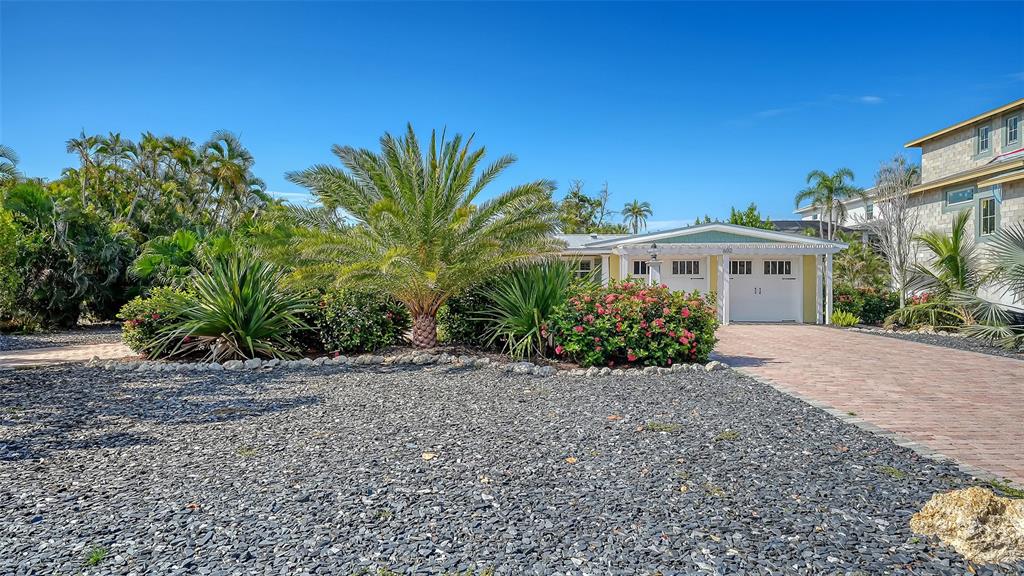 A single-story house with a white garage and a brick driveway surrounded by tropical landscaping — 602 BUTTONWOOD DRIVE, LONGBOAT KEY, FL