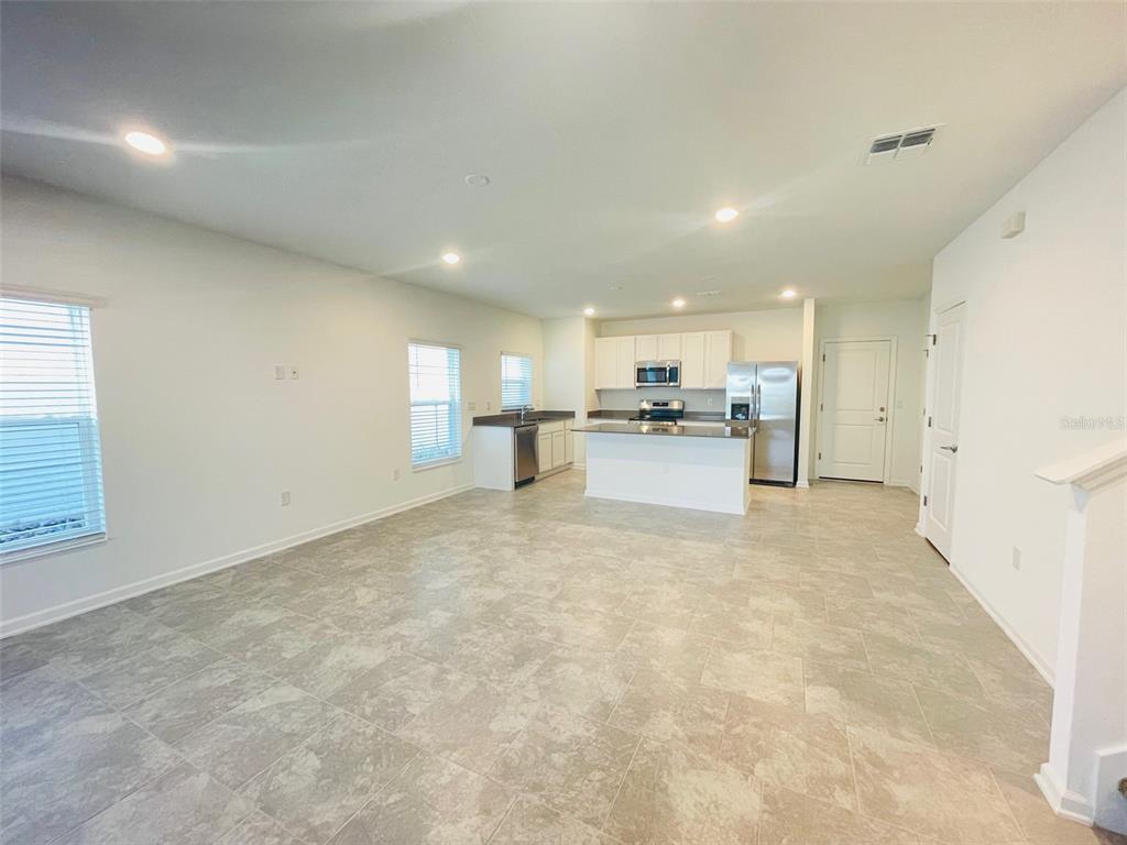 An open-concept kitchen and living area featuring white cabinetry, stainless steel appliances, and tile flooring — 6641 WILLOW VIEW AVENUE, ORLANDO, FL