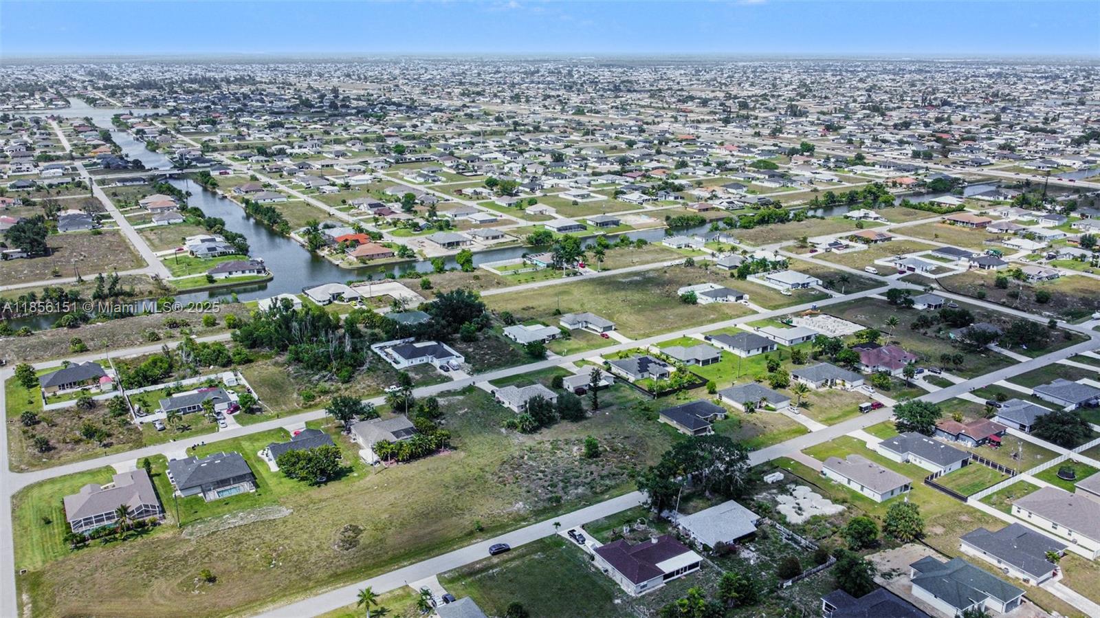 An aerial view shows a suburban neighborhood with houses, canals, and undeveloped lots — 309 NW 4th Ter, Cape Coral FL 33993, CAPE CORAL, FL