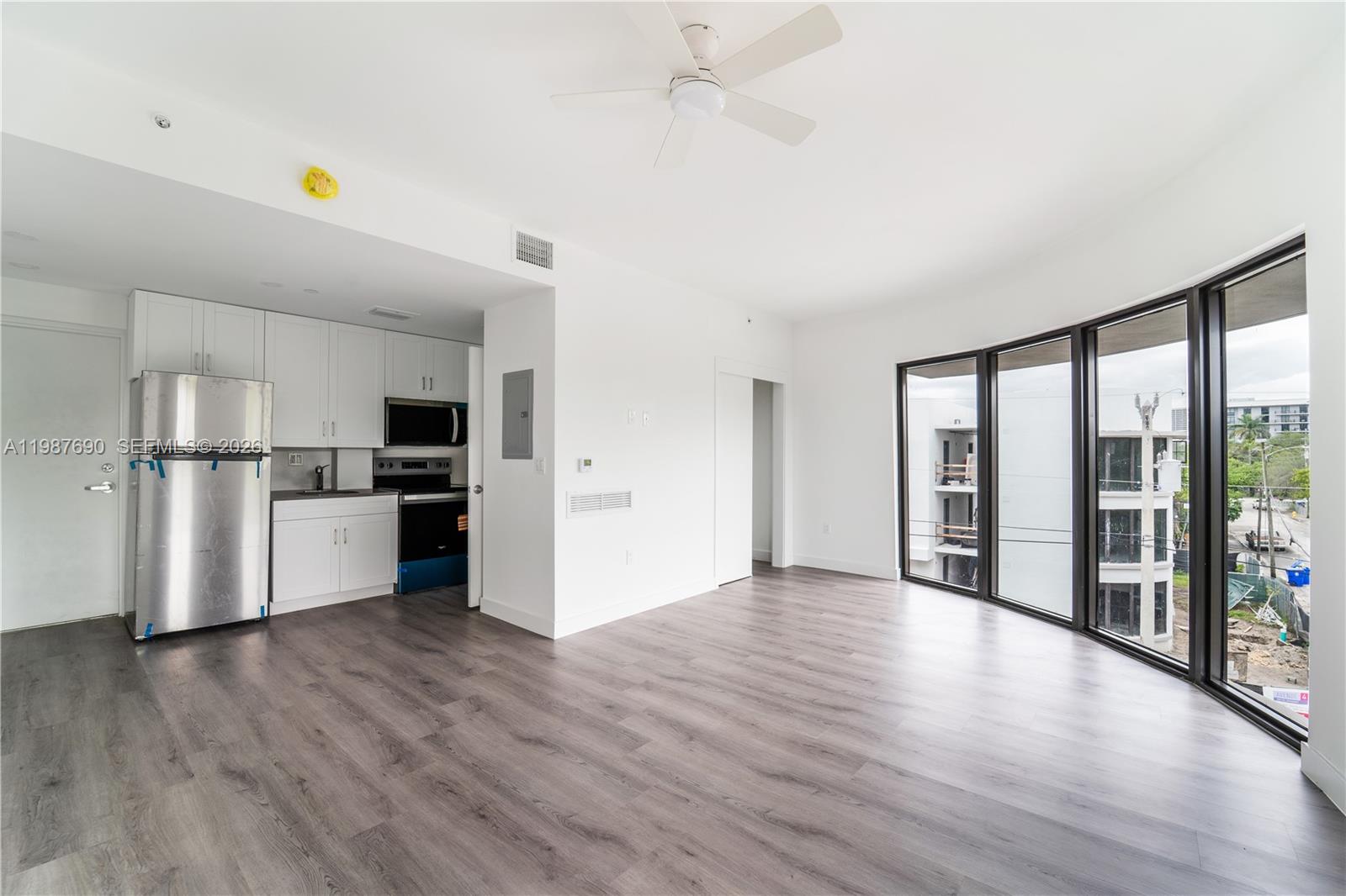 A modern studio apartment features white cabinets, stainless steel appliances, and floor-to-ceiling windows — 1165 NW 8th Ave # 104, Miami FL 33136, MIAMI, FL