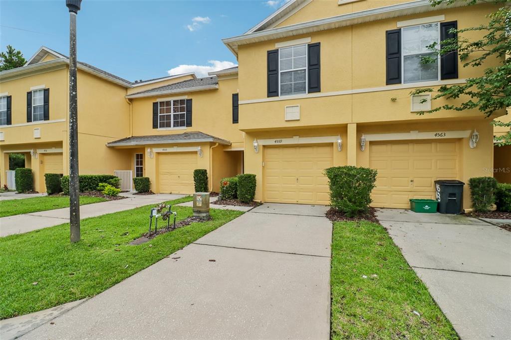 A row of yellow townhouses with attached garages and concrete driveways under a blue sky — 4559 LACEBARK TRAIL, OVIEDO, FL