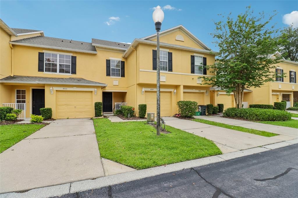 A row of yellow townhouses with attached garages and concrete driveways under a blue sky — 4559 LACEBARK TRAIL, OVIEDO, FL