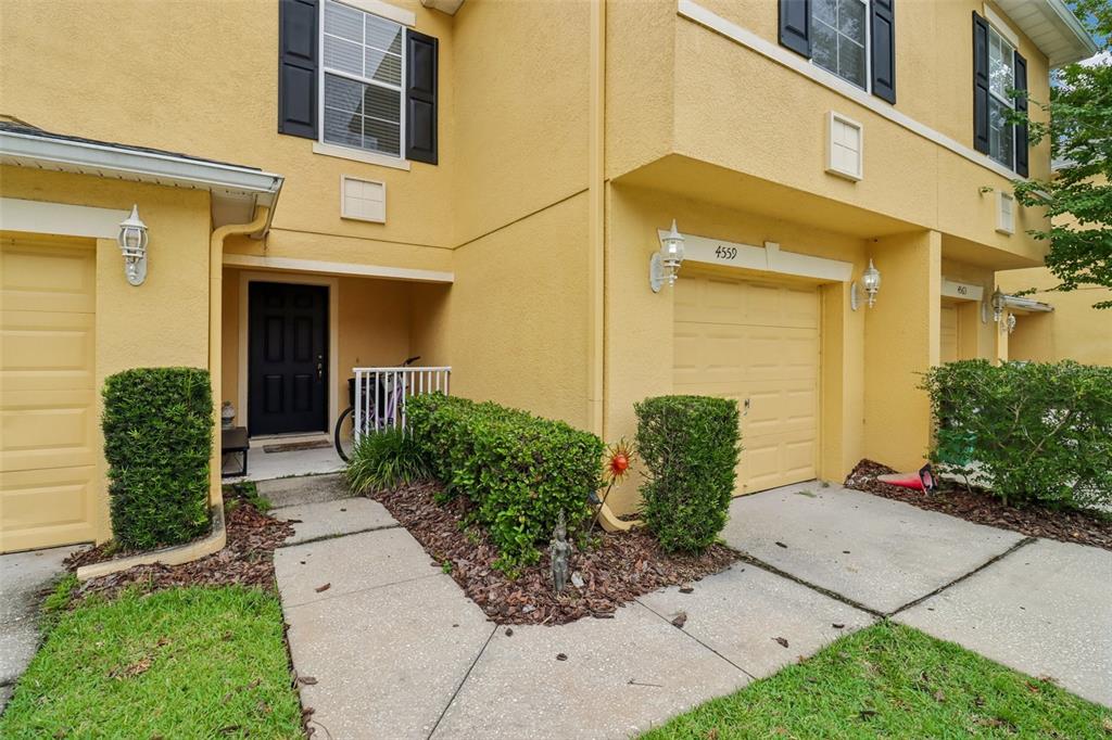 A yellow two-story townhouse exterior features a front door, a garage, and a landscaped walkway — 4559 LACEBARK TRAIL, OVIEDO, FL