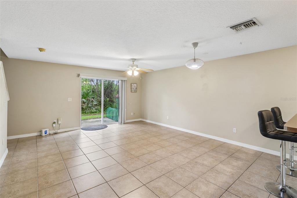 An empty living room features beige tile flooring, a ceiling fan, and sliding glass doors — 4559 LACEBARK TRAIL, OVIEDO, FL