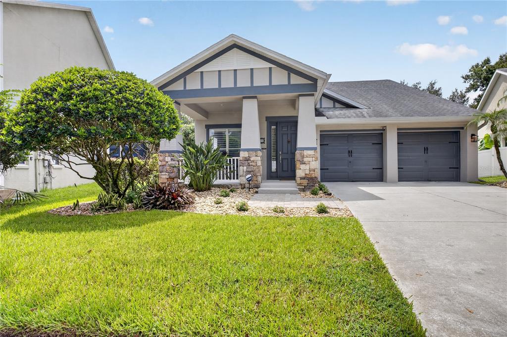 A single-story house with a stone-accented porch, gray garage doors, and a manicured lawn — 13160 SUNKISS LOOP, WINDERMERE, FL