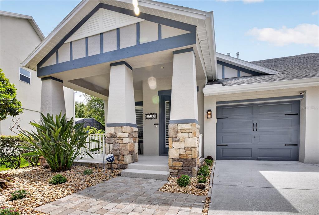 A single-story house exterior features a stone-based porch, a gray garage door, and a walkway — 13160 SUNKISS LOOP, WINDERMERE, FL