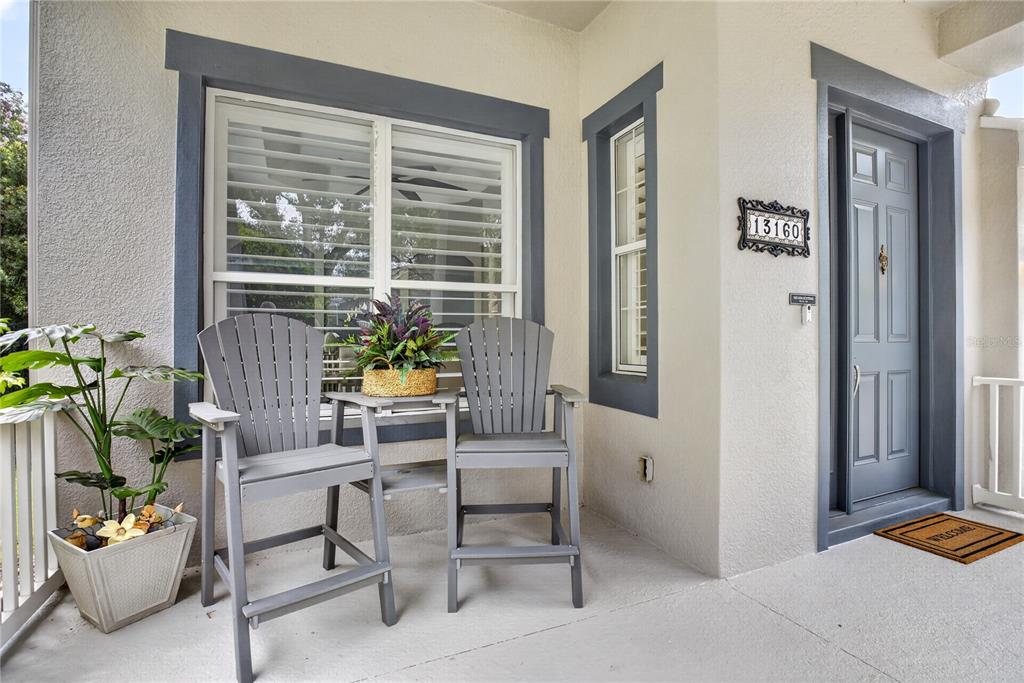 A covered front porch features two gray chairs, a small table, and a front door — 13160 SUNKISS LOOP, WINDERMERE, FL