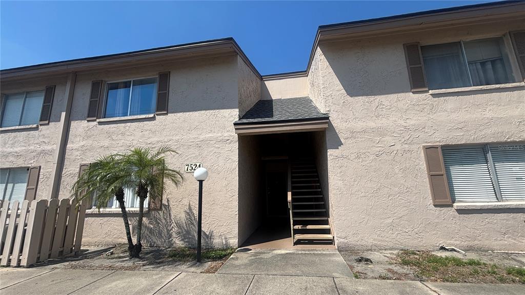 A two-story tan stucco apartment building features a central staircase leading to an entrance — 7524 NEEDLE LEAF PLACE UNIT 32, TAMPA, FL
