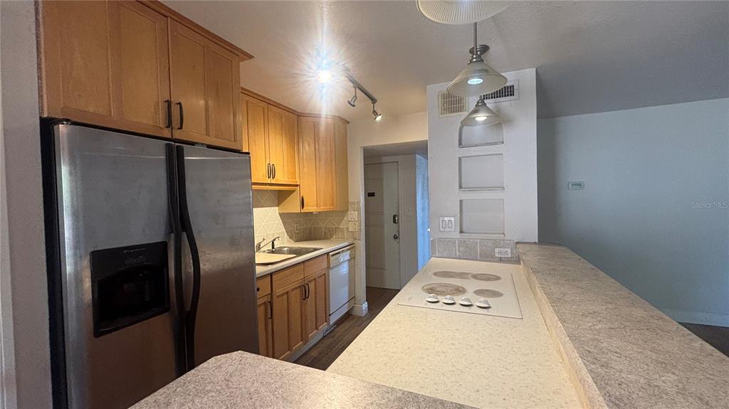 A kitchen features light wood cabinets, stainless steel appliances, and a white countertop breakfast bar — 7524 NEEDLE LEAF PLACE UNIT 32, TAMPA, FL