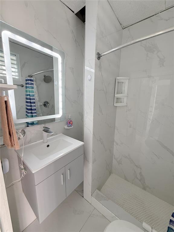 A bathroom features a gray vanity, a lighted mirror, and a walk-in shower with marble-look tiles — . BLASCOCHEA UNIT 311, CAROLINA, PR