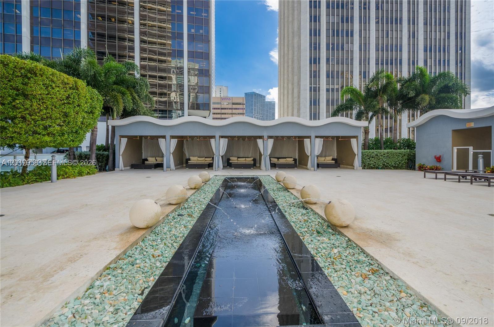 A long, narrow water feature with stone spheres sits in front of several outdoor cabanas — 50 Biscayne Blvd # 1801, Miami FL 33132, MIAMI, FL