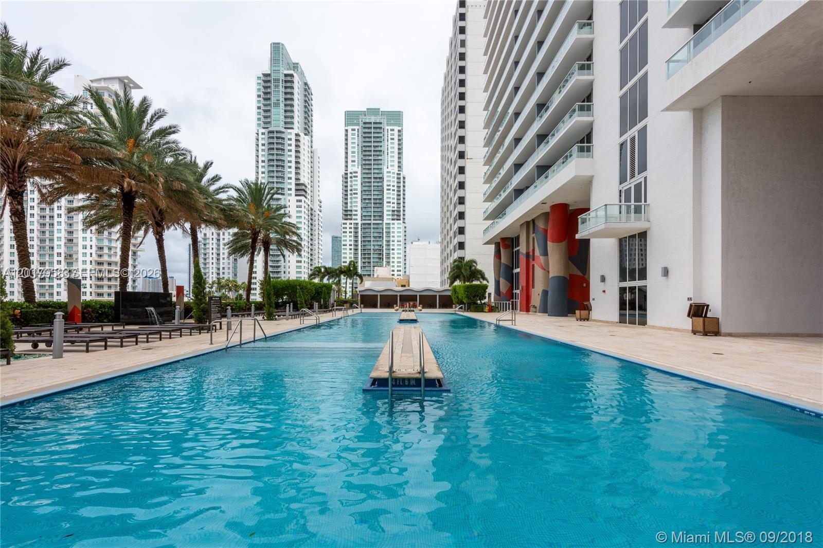 An outdoor swimming pool is situated between a tall residential building and palm trees — 50 Biscayne Blvd # 1801, Miami FL 33132, MIAMI, FL