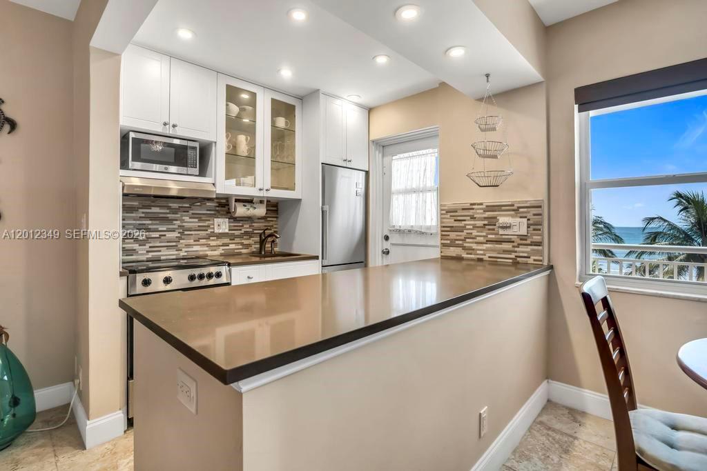 A kitchen features white cabinets, a brown countertop, a tiled backsplash, and an ocean view — 901 S Surf Rd # 404, Hollywood FL 33019, HOLLYWOOD, FL