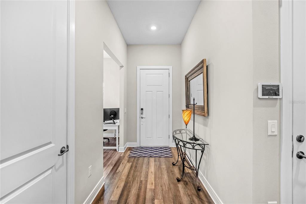 A hallway with wood-look flooring leads to a white door, a console table, and mirror — 9336 SW 56TH LOOP, OCALA, FL