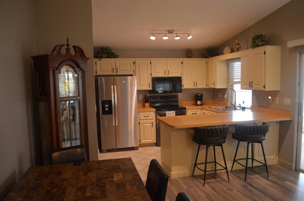 A kitchen features cream cabinets, stainless steel appliances, a wooden breakfast bar, and tile flooring — 6625 GASPARILLA PINES BOULEVARD, ENGLEWOOD, FL