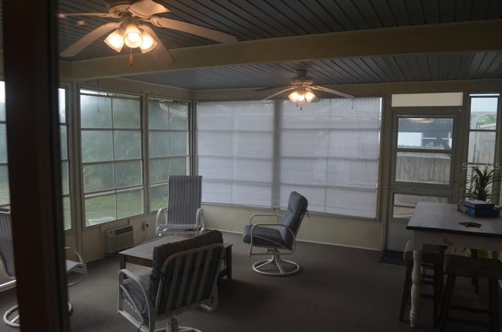 A sunroom features carpeted floors, two ceiling fans, large windows, and casual patio furniture — 6625 GASPARILLA PINES BOULEVARD, ENGLEWOOD, FL