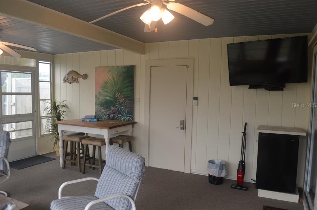 A sunroom features a ceiling fan, a wall-mounted television, a small table, and a door — 6625 GASPARILLA PINES BOULEVARD, ENGLEWOOD, FL
