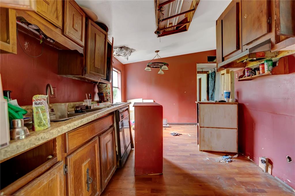 A dilapidated kitchen features red walls, wooden cabinets, and damaged ceiling panels — 6602 BROOKRIDGE TRAIL, LAKELAND, FL