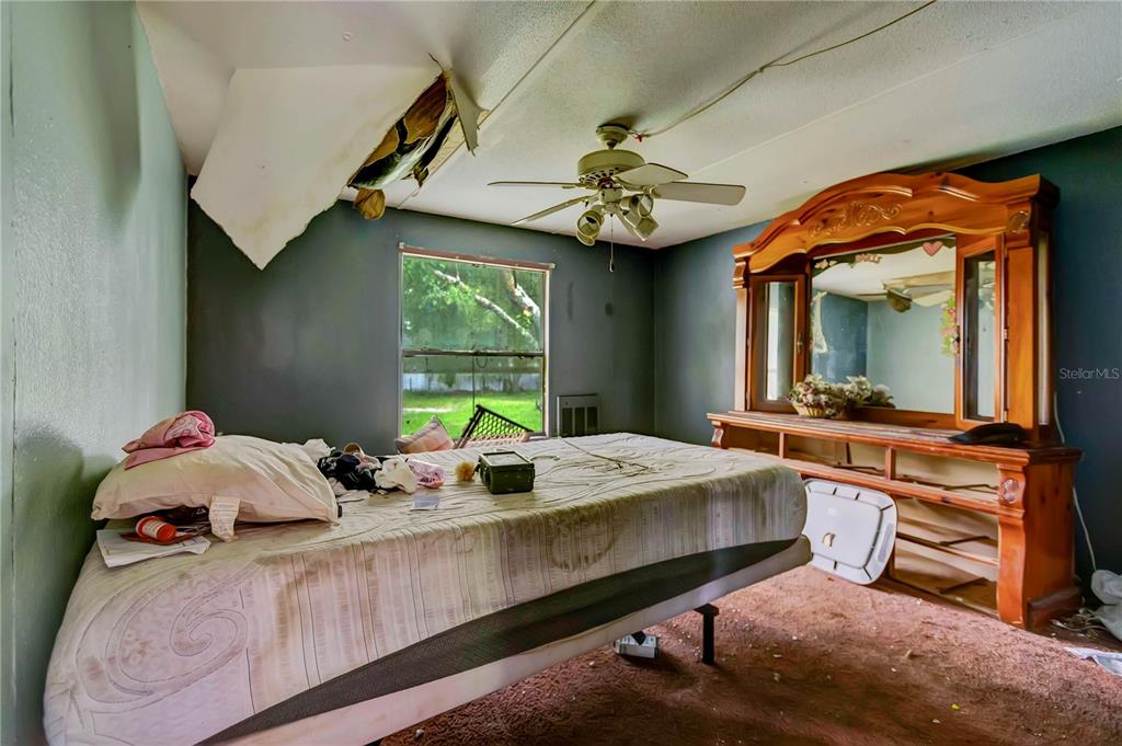 A bedroom with a damaged ceiling, a ceiling fan, a bed, and a wooden dresser — 6602 BROOKRIDGE TRAIL, LAKELAND, FL