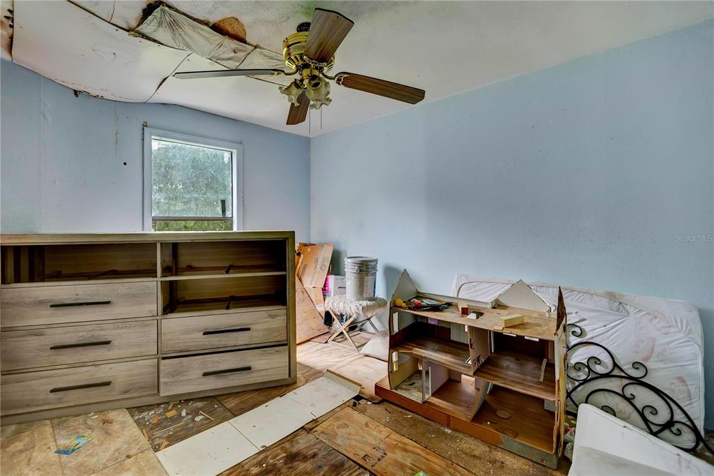 A bedroom with a damaged ceiling, a dresser, a dollhouse, and exposed subflooring — 6602 BROOKRIDGE TRAIL, LAKELAND, FL