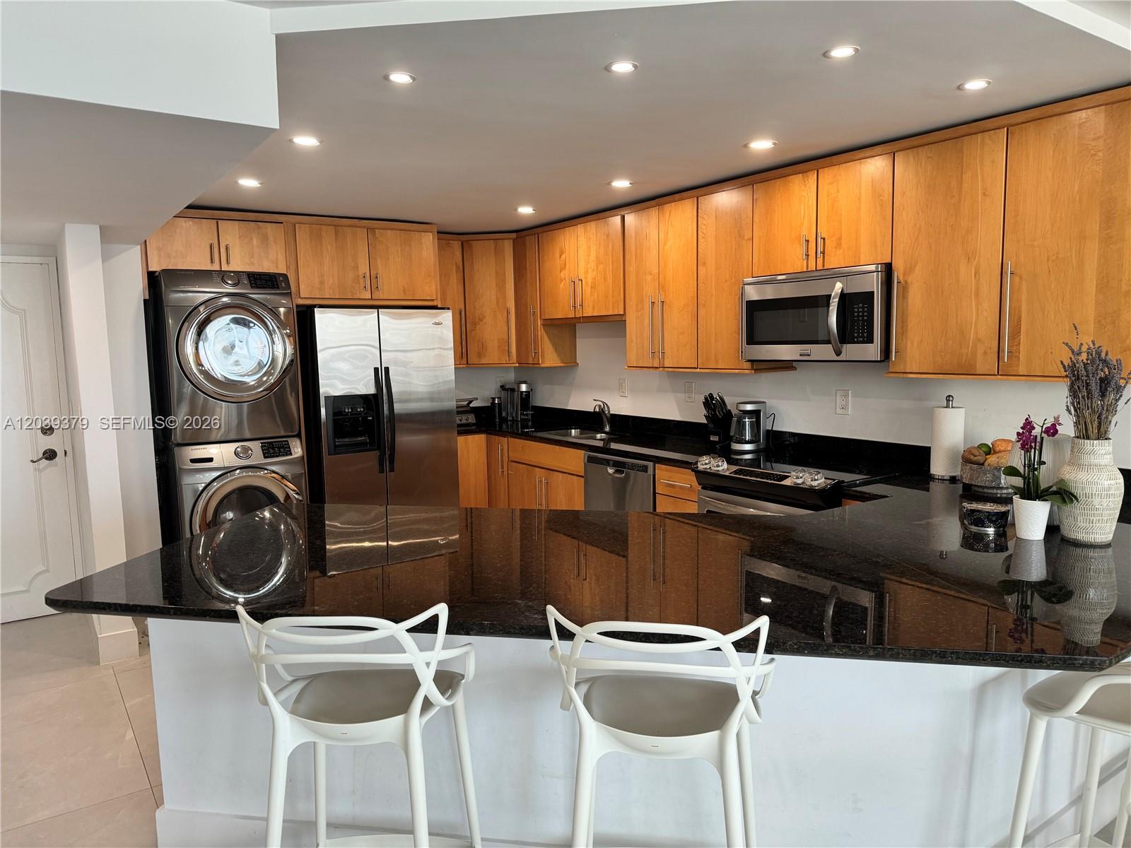 A kitchen features light wood cabinets, black granite countertops, stainless steel appliances, and white barstools — 1865 Brickell Ave # A1411, Miami FL 33129, MIAMI, FL