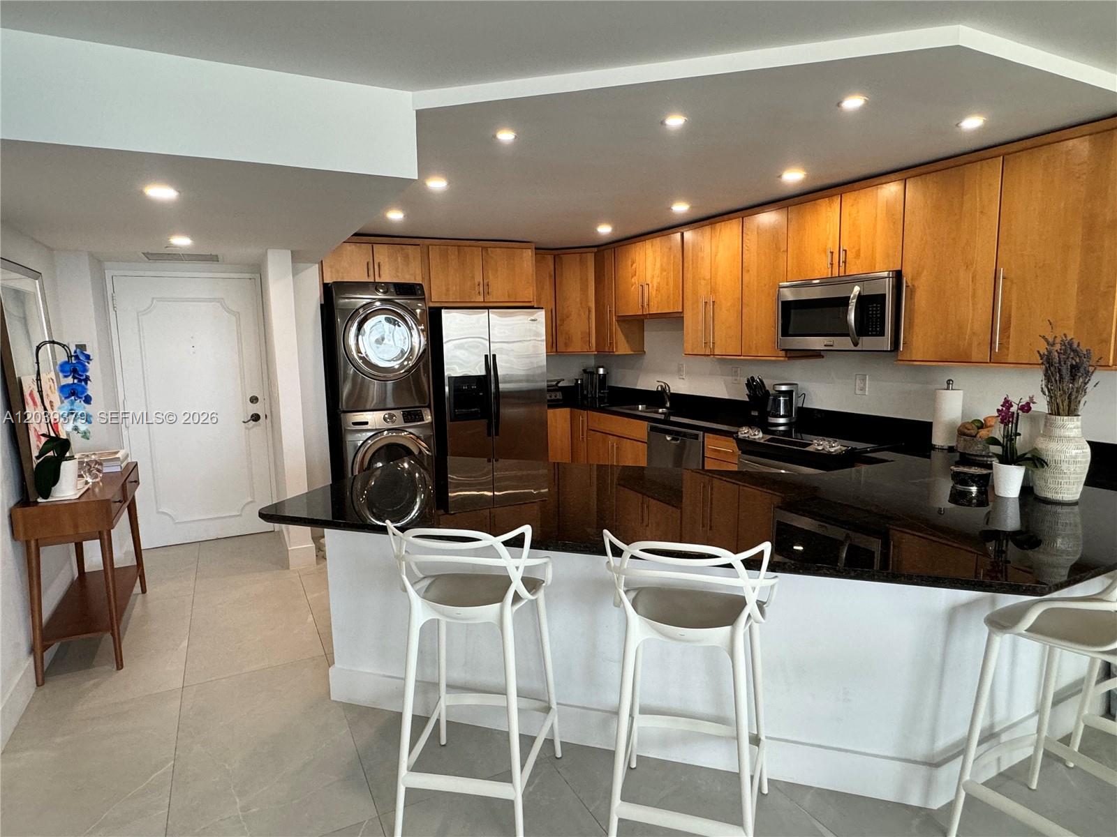 A kitchen features light wood cabinets, black granite countertops, stainless steel appliances, and white stools — 1865 Brickell Ave # A1411, Miami FL 33129, MIAMI, FL