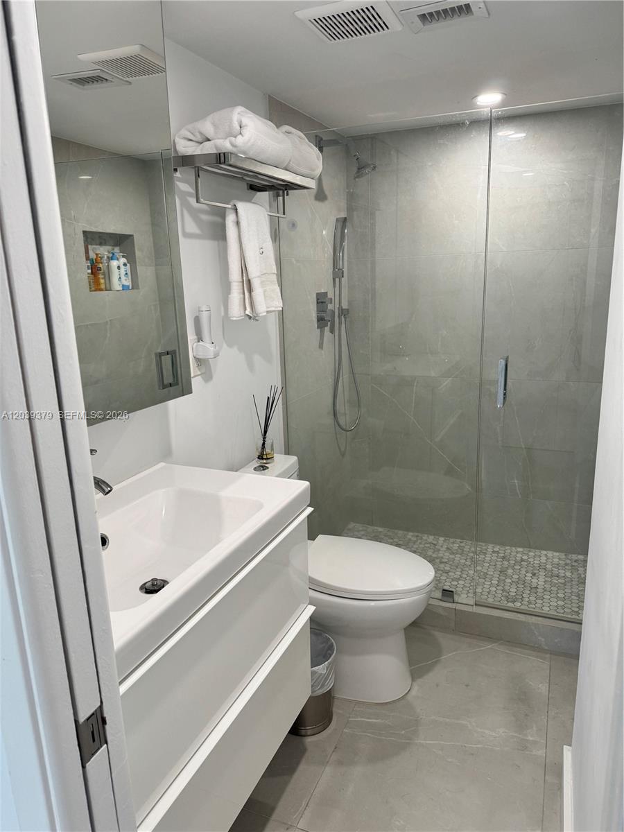 A modern bathroom features a white vanity, a glass-enclosed shower, and light-colored tile flooring — 1865 Brickell Ave # A1411, Miami FL 33129, MIAMI, FL