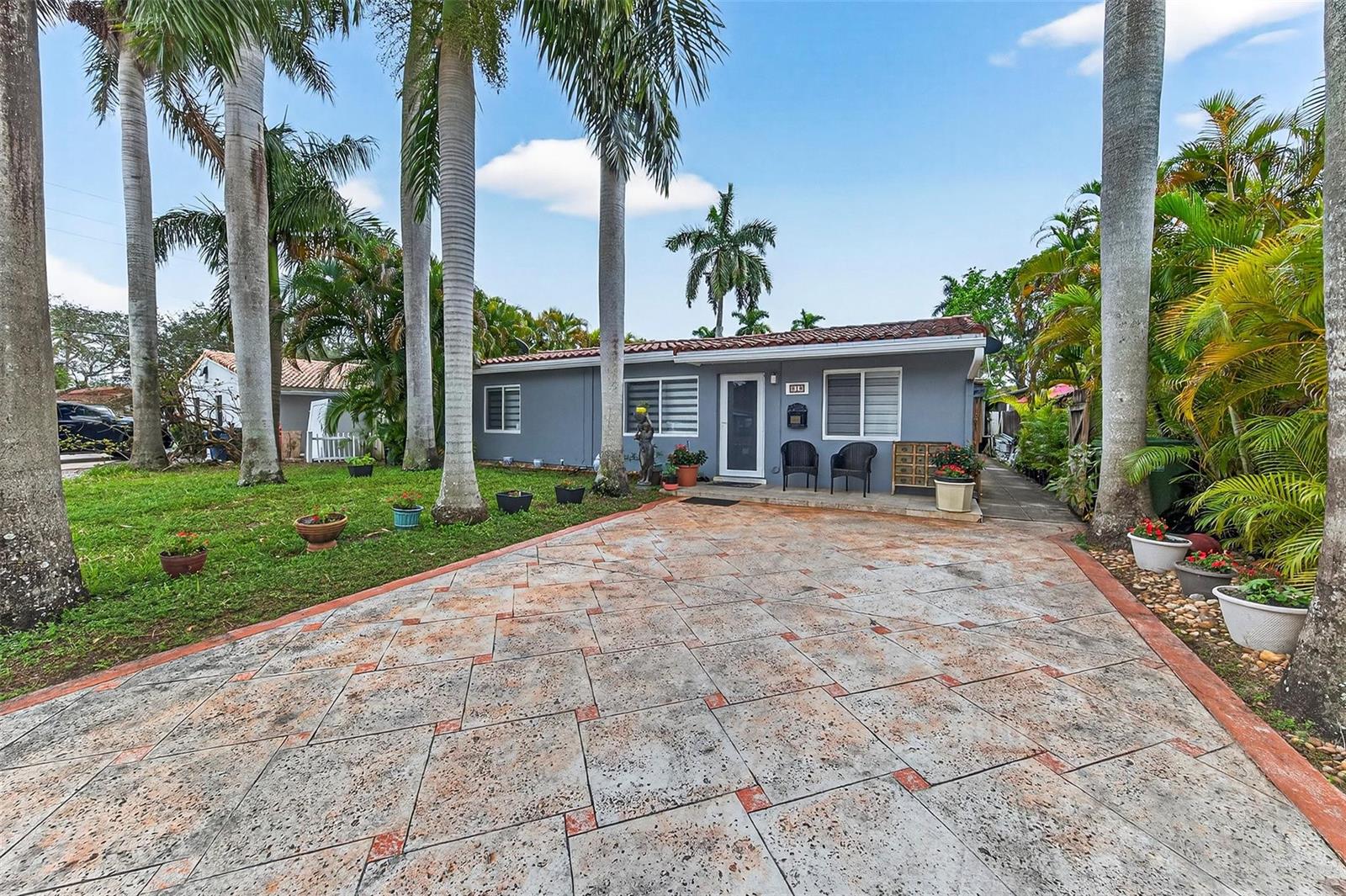 A gray single-story house features a patterned concrete driveway and several tall palm trees — 918 NE 4th Street, Hallandale Beach FL 33009, HALLANDALE BEACH, FL