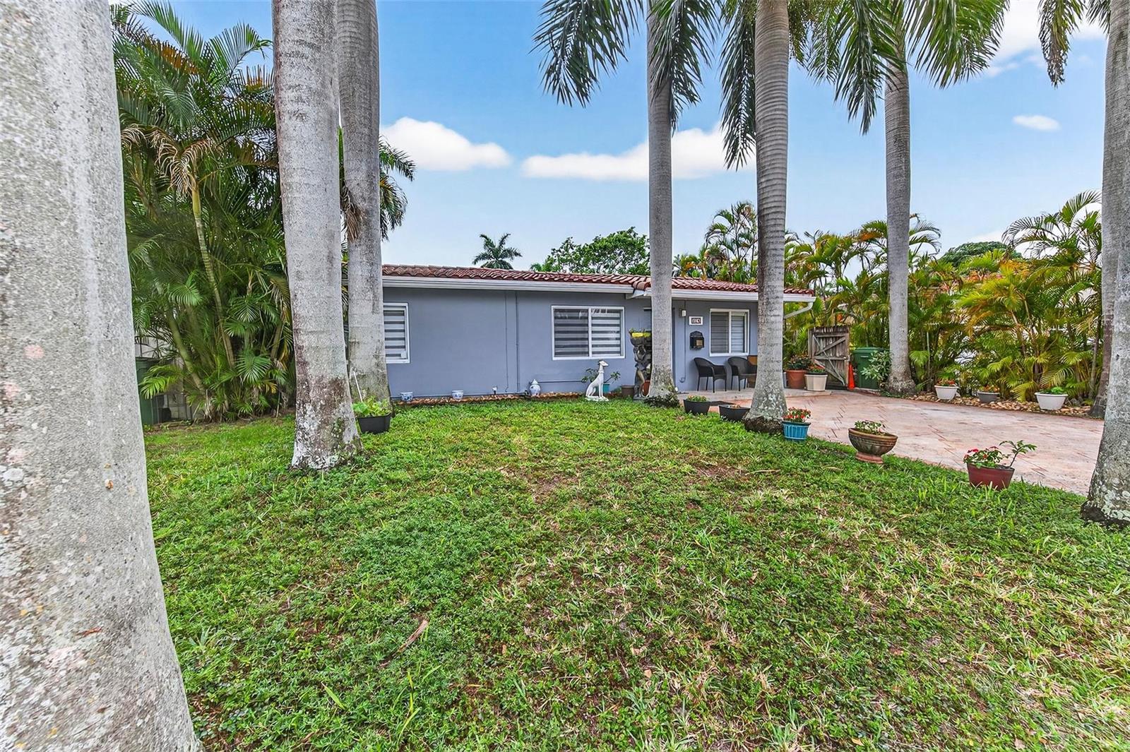 A single-story gray house with a tiled roof sits behind a grassy yard and palm trees — 918 NE 4th Street, Hallandale Beach FL 33009, HALLANDALE BEACH, FL