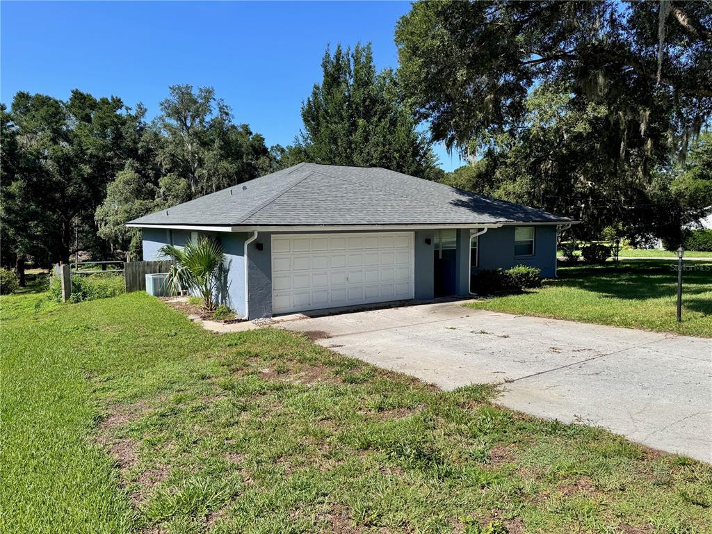 A blue single-story house features a two-car garage, a concrete driveway, and surrounding trees — 8114 E DECATUR COURT, FLORAL CITY, FL