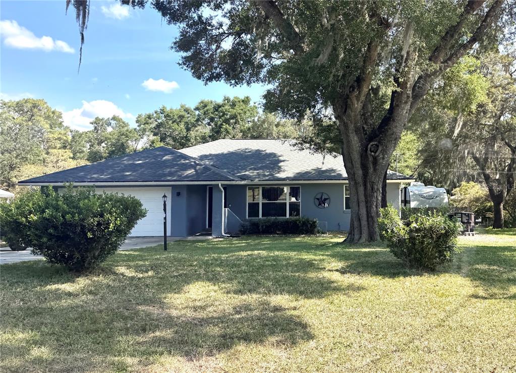 A single-story house with a gray exterior, a white garage door, and a large tree — 8114 E DECATUR COURT, FLORAL CITY, FL