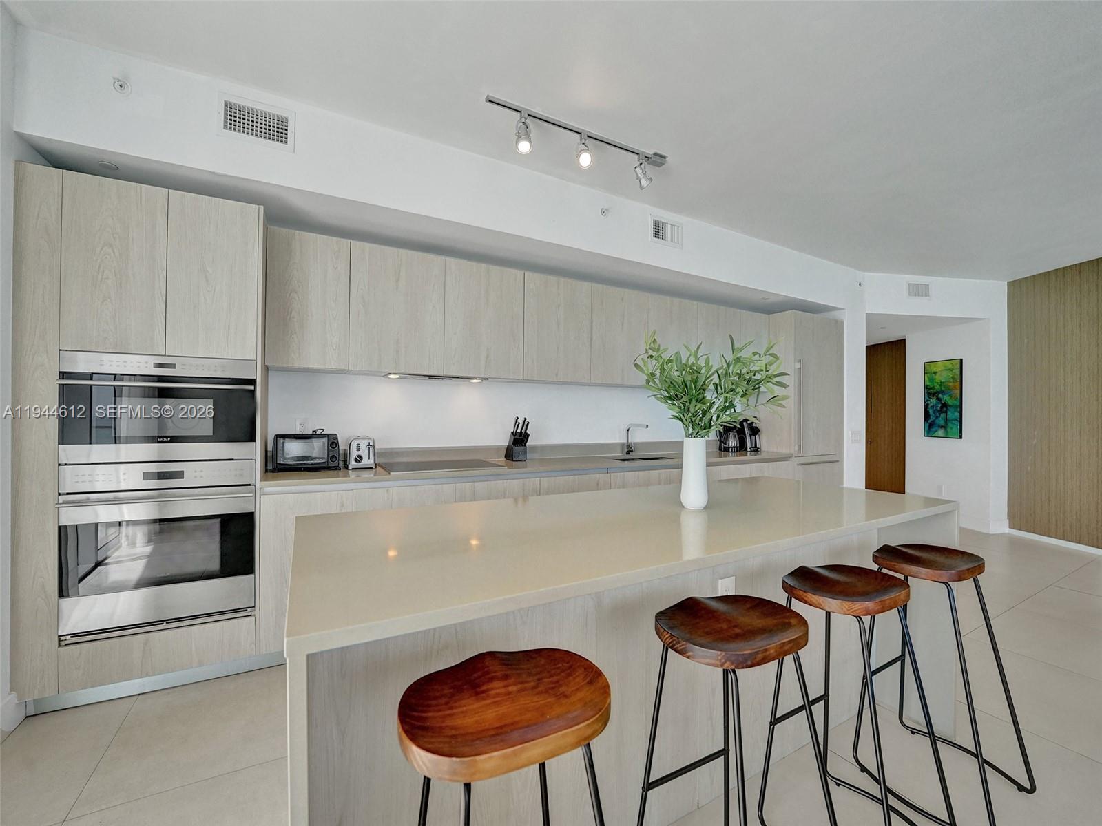 A modern kitchen features light wood cabinetry, a large quartz island, and three wooden stools — 4111 S Ocean Dr # 1201, Hollywood FL 33019, HOLLYWOOD, FL