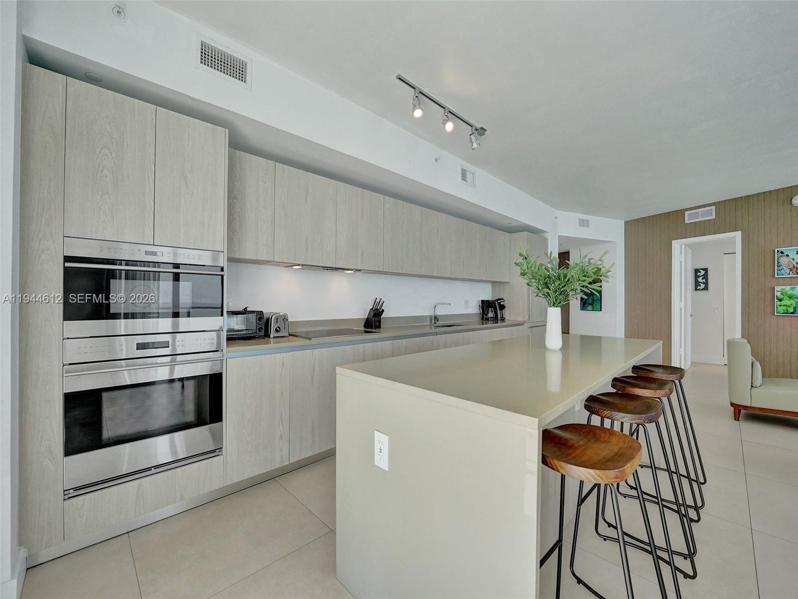 A modern kitchen features light wood cabinetry, a large island with bar stools, and stainless appliances — 4111 S Ocean Dr # 1201, Hollywood FL 33019, HOLLYWOOD, FL