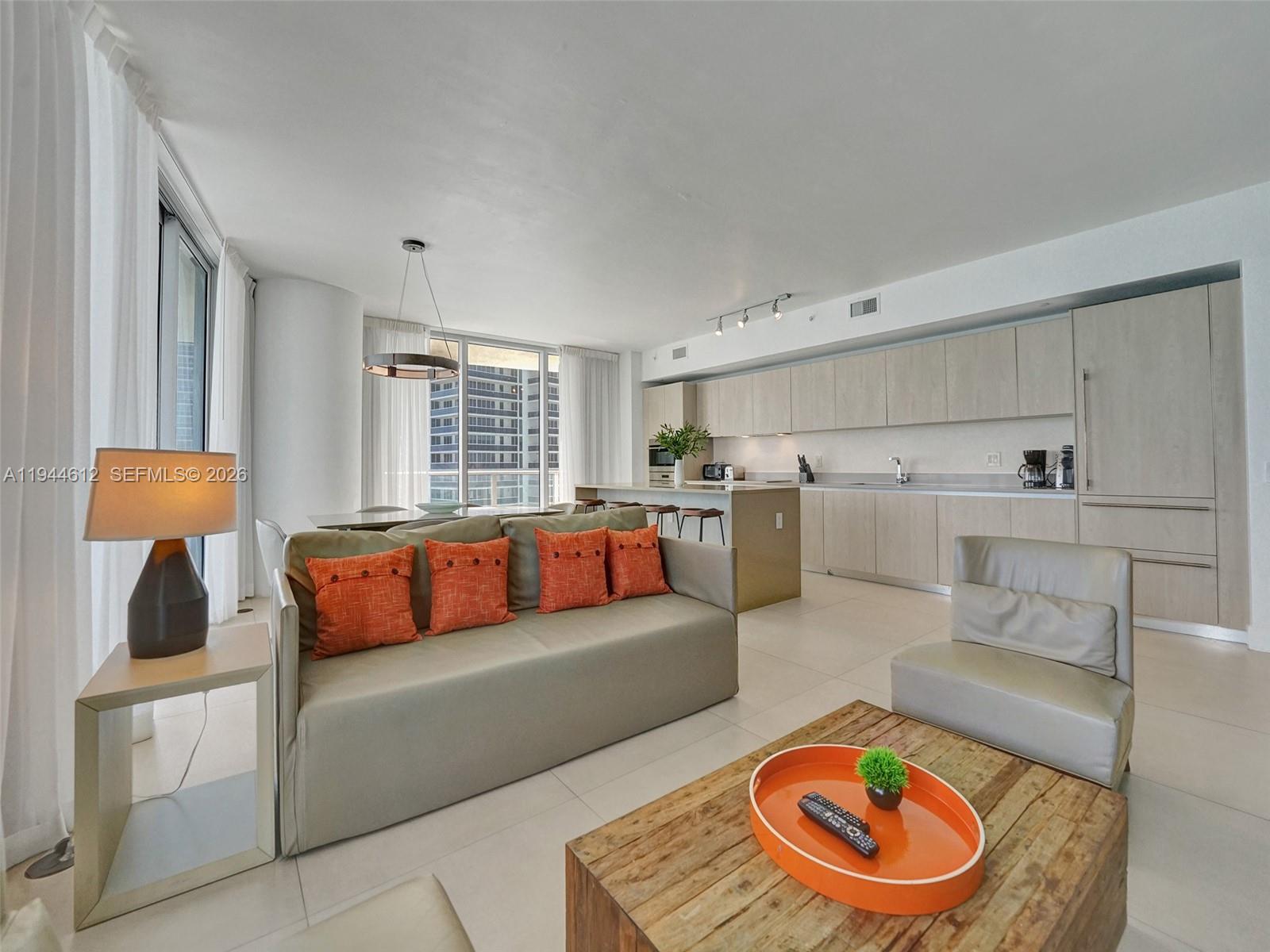 A modern open-concept living room features a sofa with orange pillows and a kitchen area — 4111 S Ocean Dr # 1201, Hollywood FL 33019, HOLLYWOOD, FL