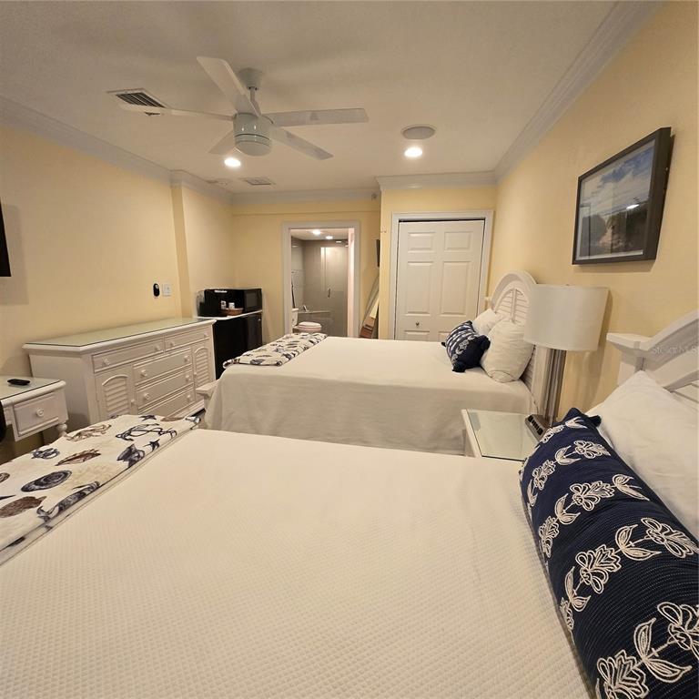 A bedroom with two beds, a white dresser, a ceiling fan, and an attached bathroom — 36750 US HIGHWAY 19 N UNIT 11-104, PALM HARBOR, FL
